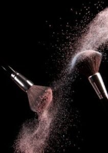 High-speed capture of makeup brushes dispersing pink powder in motion against a dark background.