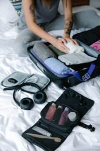 Person organizing suitcase with clothes and toiletries on bed, preparing for travel.